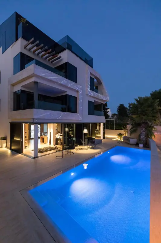 Bâtiment moderne éclairé avec une piscine au premier plan.