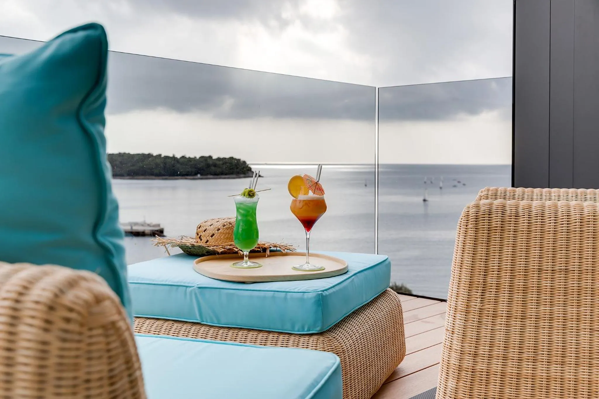Deux cocktails colorés reposent sur une table basse devant une vue sur la mer.