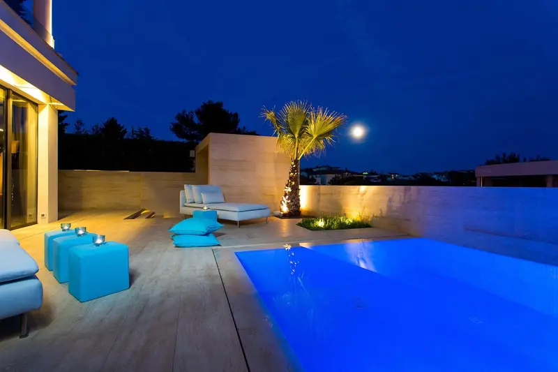Terrasse avec piscine et mobilier lumineux sous un ciel nocturne.