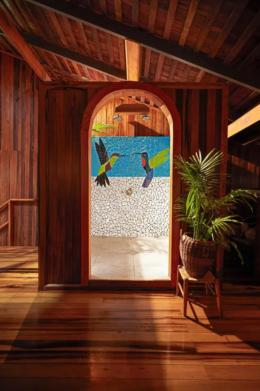 Une arche en bois donne sur une salle de bain lumineuse avec une mosaïque colorée.