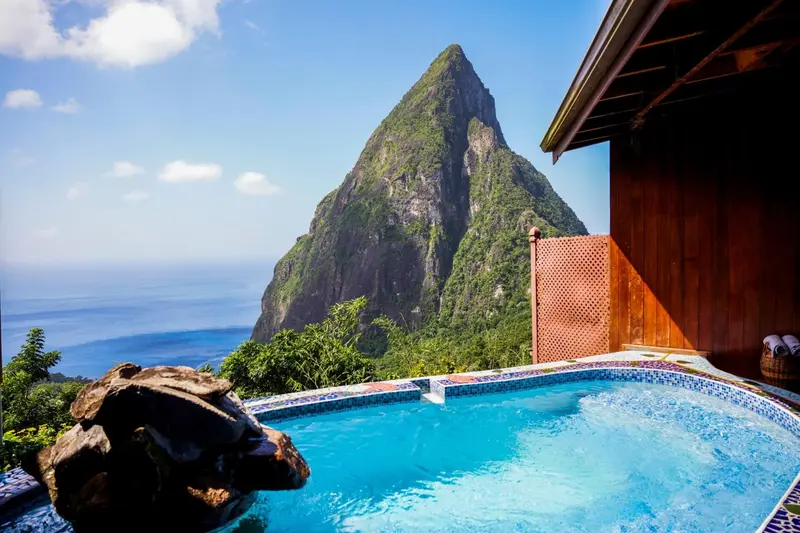 Une piscine à débordement offre une vue sur une montagne verdoyante et la mer.