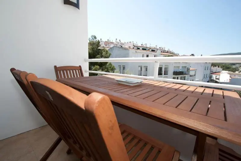 Table et chaises en bois sur une terrasse ensoleillée avec vue sur la ville.