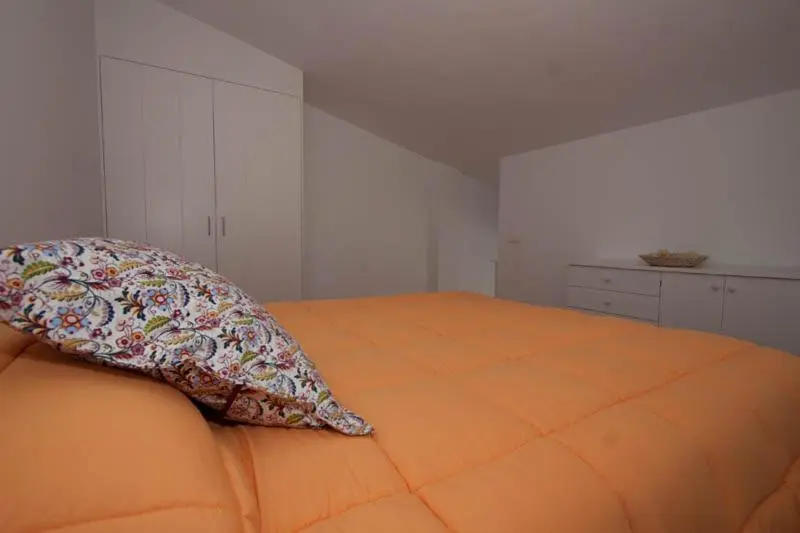 Une chambre lumineuse avec un lit recouvert d'une couverture orange et d'un coussin fleuri.