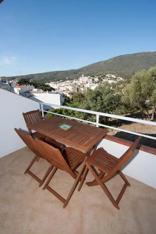 Table et chaises en bois sur une terrasse avec vue sur un village et des collines.
