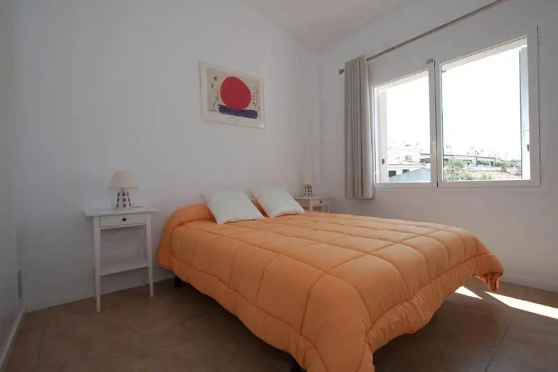 Une chambre lumineuse avec un lit recouvert d'une couverture orange et un tableau au mur.
