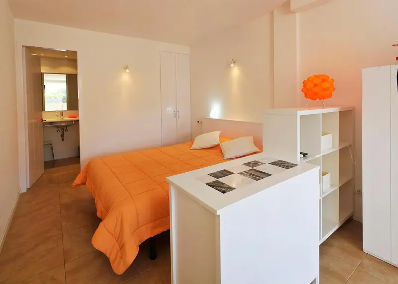 Une chambre lumineuse avec un lit recouvert d'une couverture orange et un espace détente.