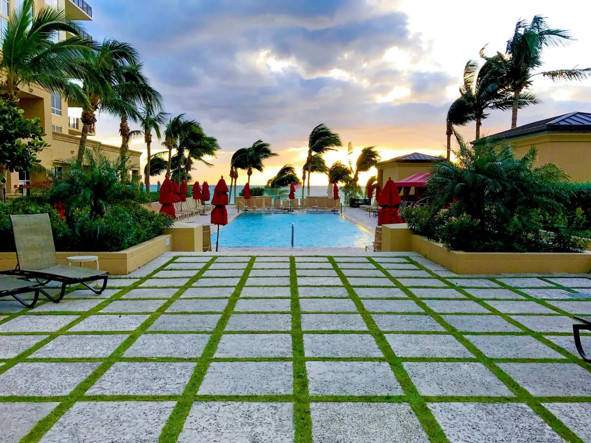 Une piscine bordée de transats et de végétation, avec un coucher de soleil en arrière-plan.