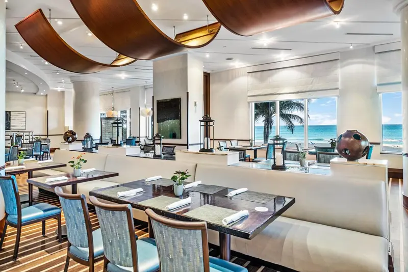 Une salle de restaurant lumineuse avec des tables dressées et une vue sur la mer.