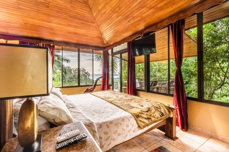 Une chambre lumineuse avec un lit recouvert d'une courtepointe et une vue sur la végétation.