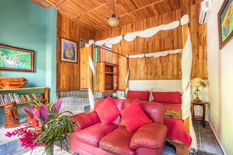 Une chambre aux murs en bois et au lit à baldaquin rouge est aménagée avec un canapé et une bibliothèque.