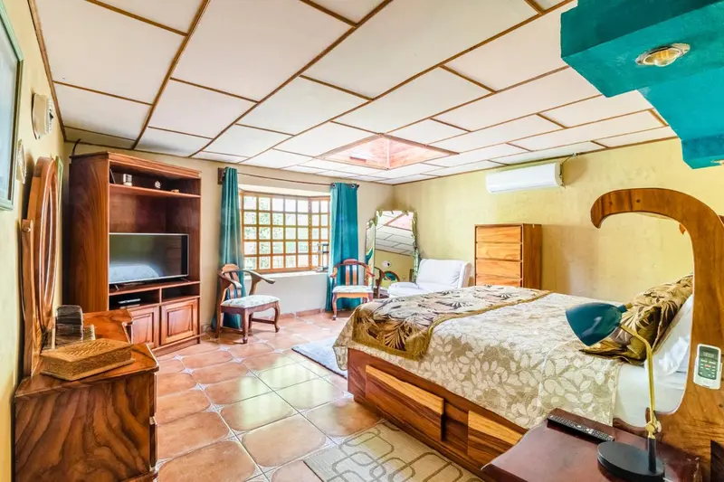 Une chambre lumineuse avec un lit recouvert d'une courtepointe et un meuble télévision.