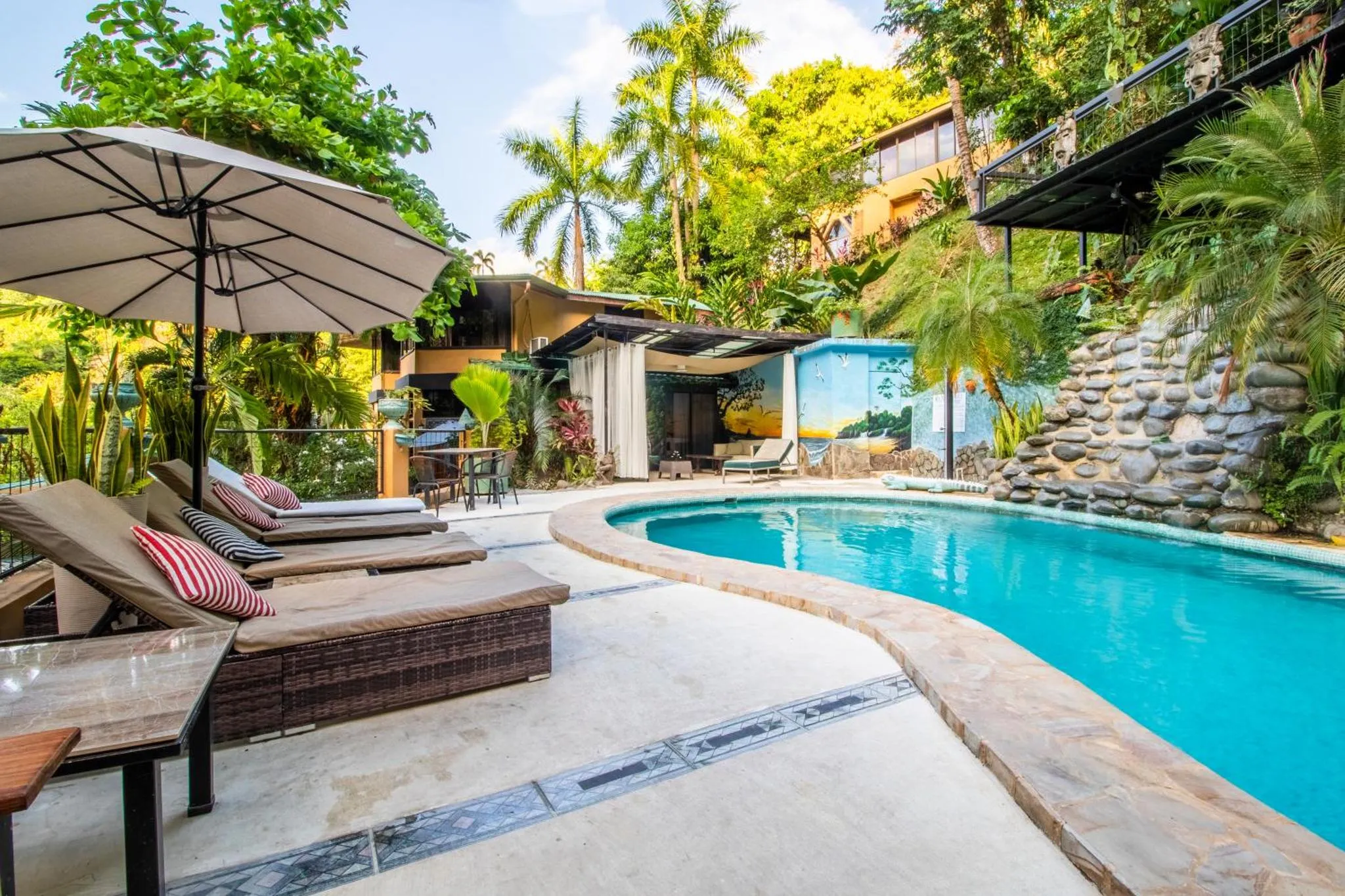 Transats et parasol bordent une piscine turquoise dans un cadre tropical.