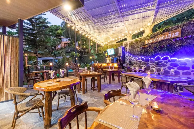 Une salle à manger extérieure avec des tables en bois éclairées par des guirlandes lumineuses.