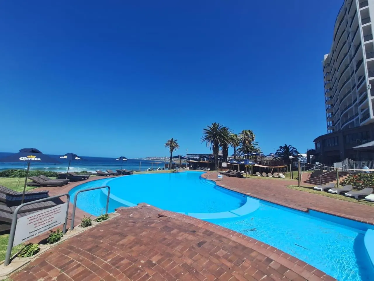 Une piscine turquoise bordée d'une terrasse ensoleillée avec des transats.
