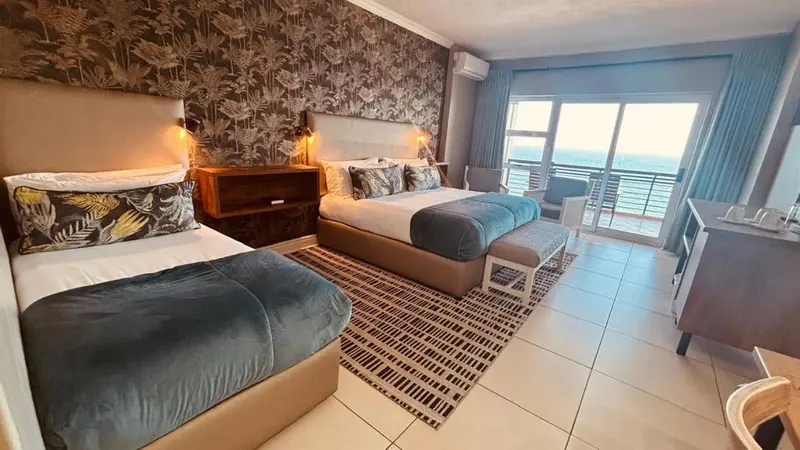 Chambre avec deux lits et vue sur la mer par une baie vitrée.