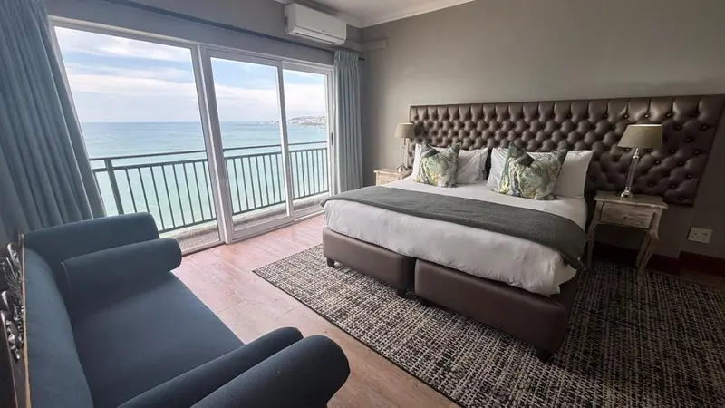 Une chambre avec un grand lit face à une baie vitrée donnant sur la mer.