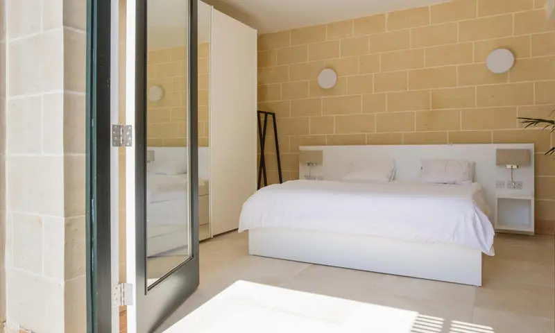 Une chambre lumineuse avec un grand lit blanc et des murs jaunes.