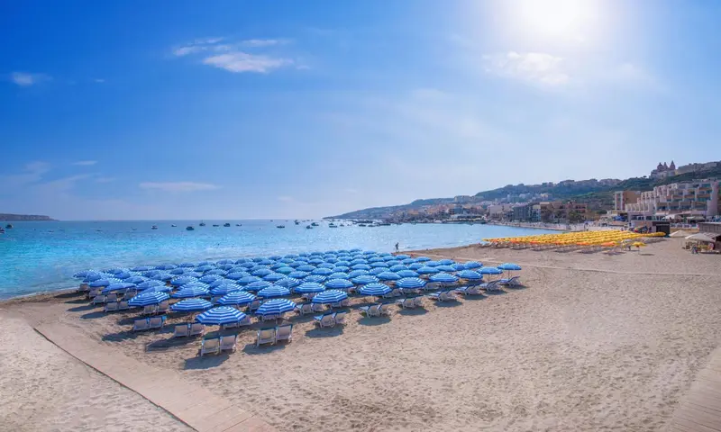 Plage de sable fin avec transats et parasols bleus sous un ciel clair.