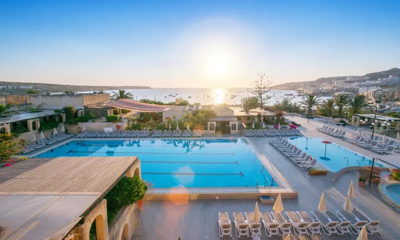Vue aérienne d'une piscine d'hôtel avec des transats et la mer en arrière-plan.