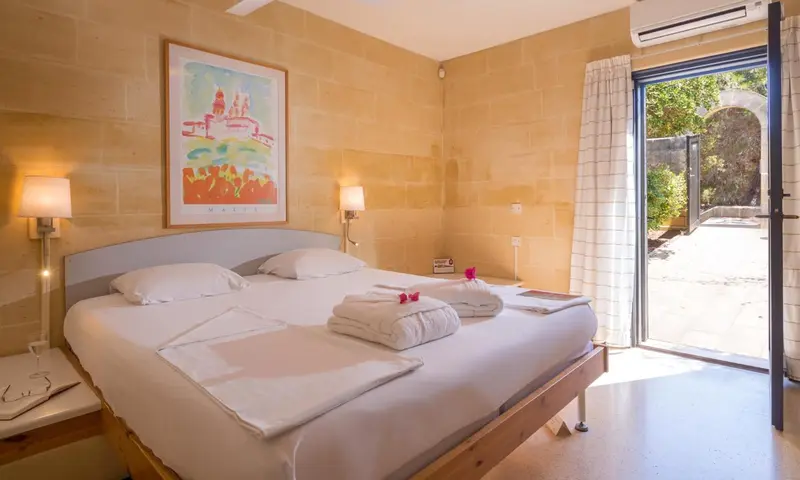 Une chambre lumineuse avec un grand lit et une porte-fenêtre ouverte sur une cour.