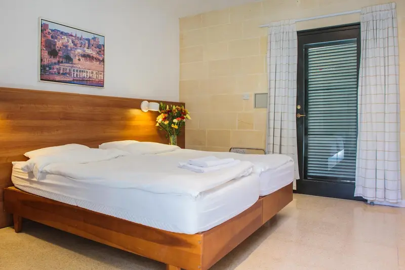 Une chambre lumineuse avec un grand lit et un bouquet de fleurs.