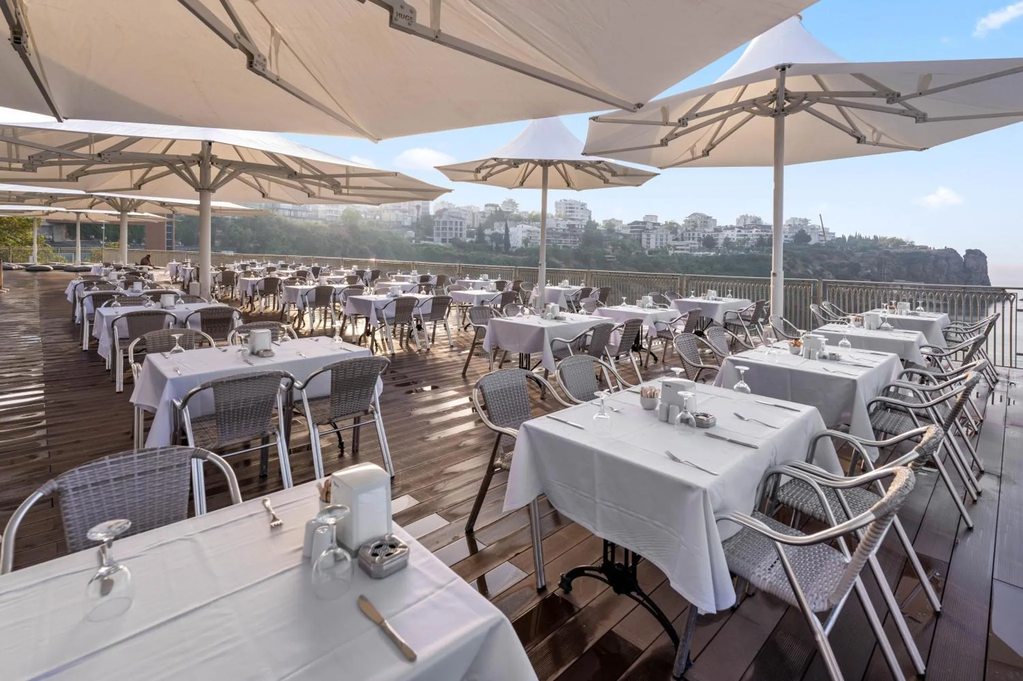 Terrasse ombragée avec tables nappées et vue sur la mer.