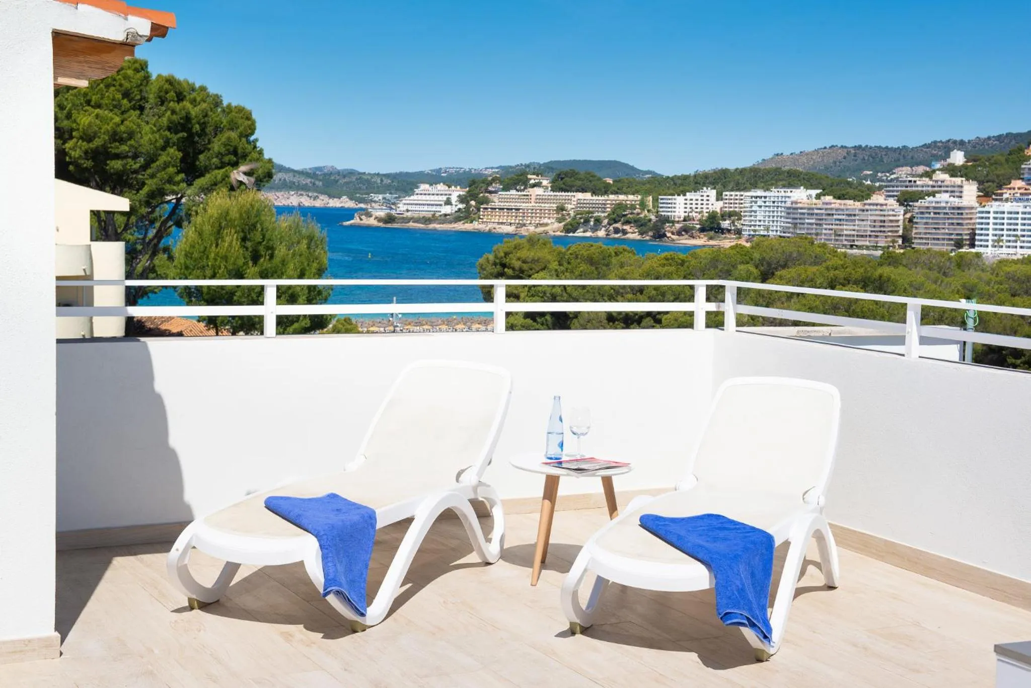 Deux transats bleus sur une terrasse ensoleillée avec vue sur la mer et la côte.