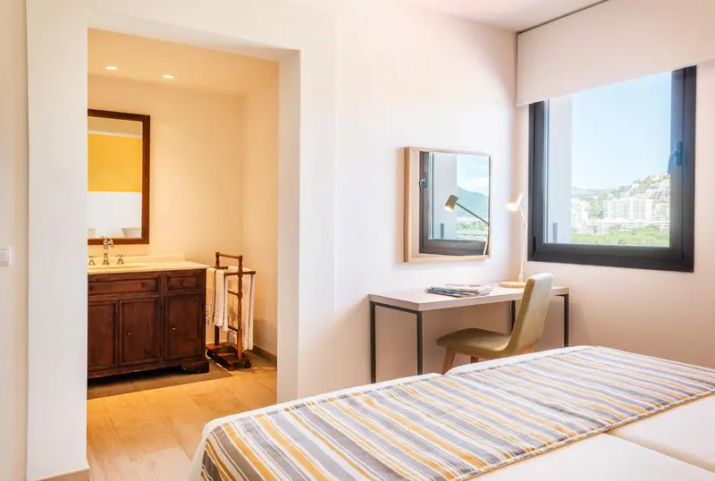 Une chambre lumineuse avec un coin bureau et une salle de bain attenante.