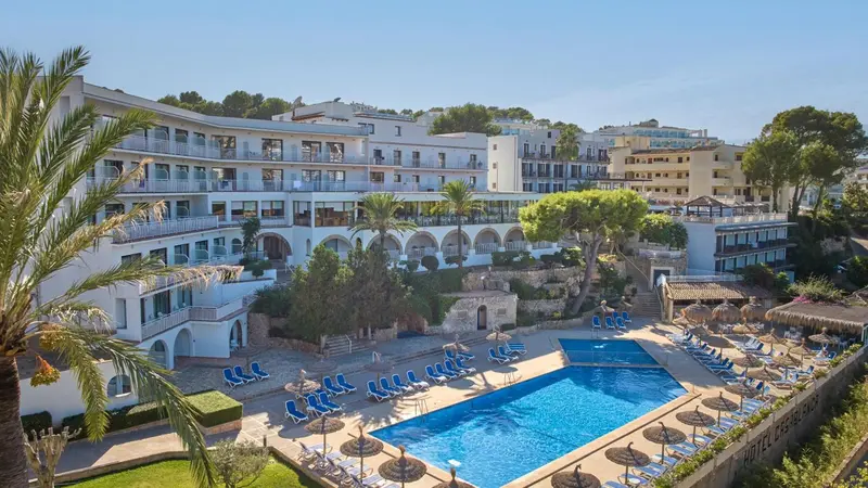 Vue aérienne d'un bâtiment blanc avec des balcons surplombant une piscine et une plage.