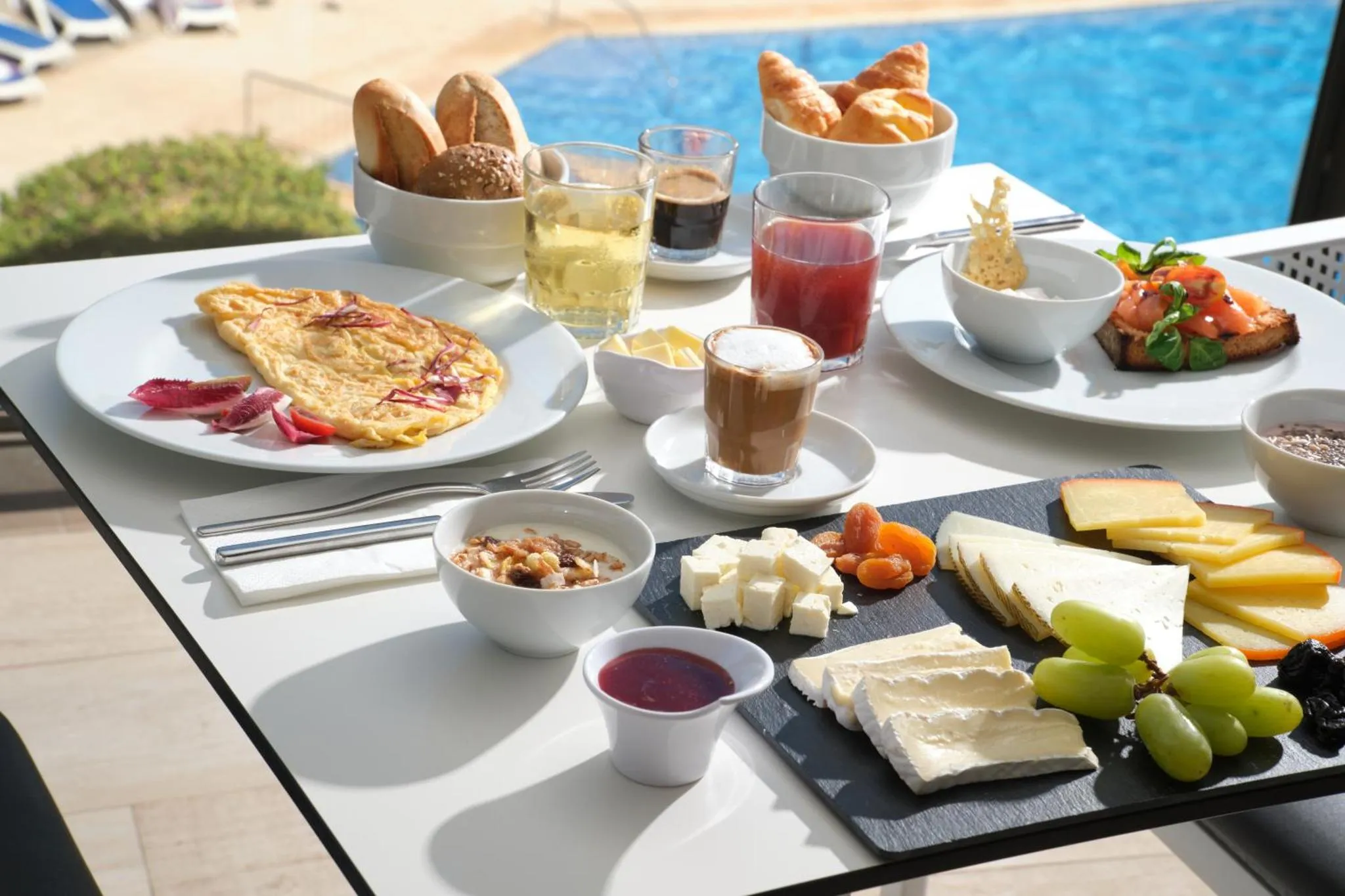 Une table blanche est dressée avec un copieux petit-déjeuner composé de viennoiseries, d'œufs, de fruits et de boissons.