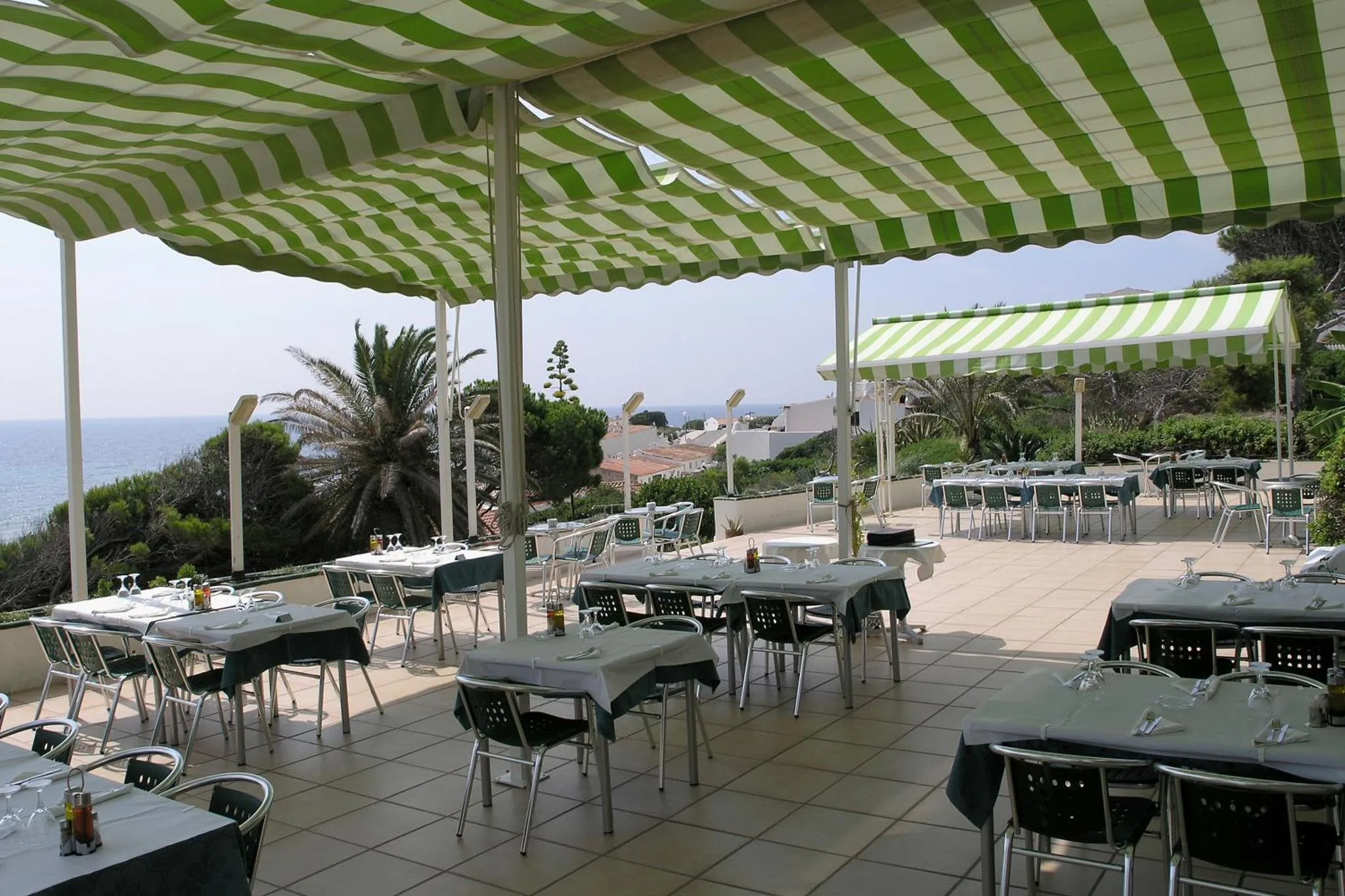 Terrasse ombragée avec tables et chaises donnant sur la mer.