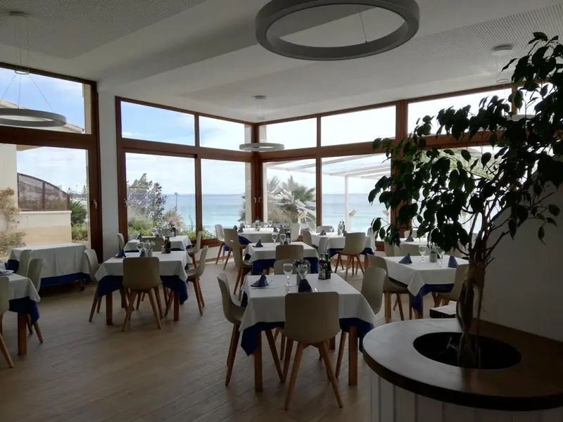 Une salle lumineuse avec de grandes baies vitrées donnant sur la mer et des tables dressées pour un repas.