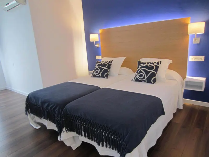 Une chambre lumineuse avec un grand lit recouvert d'une couverture bleu foncé et de coussins.