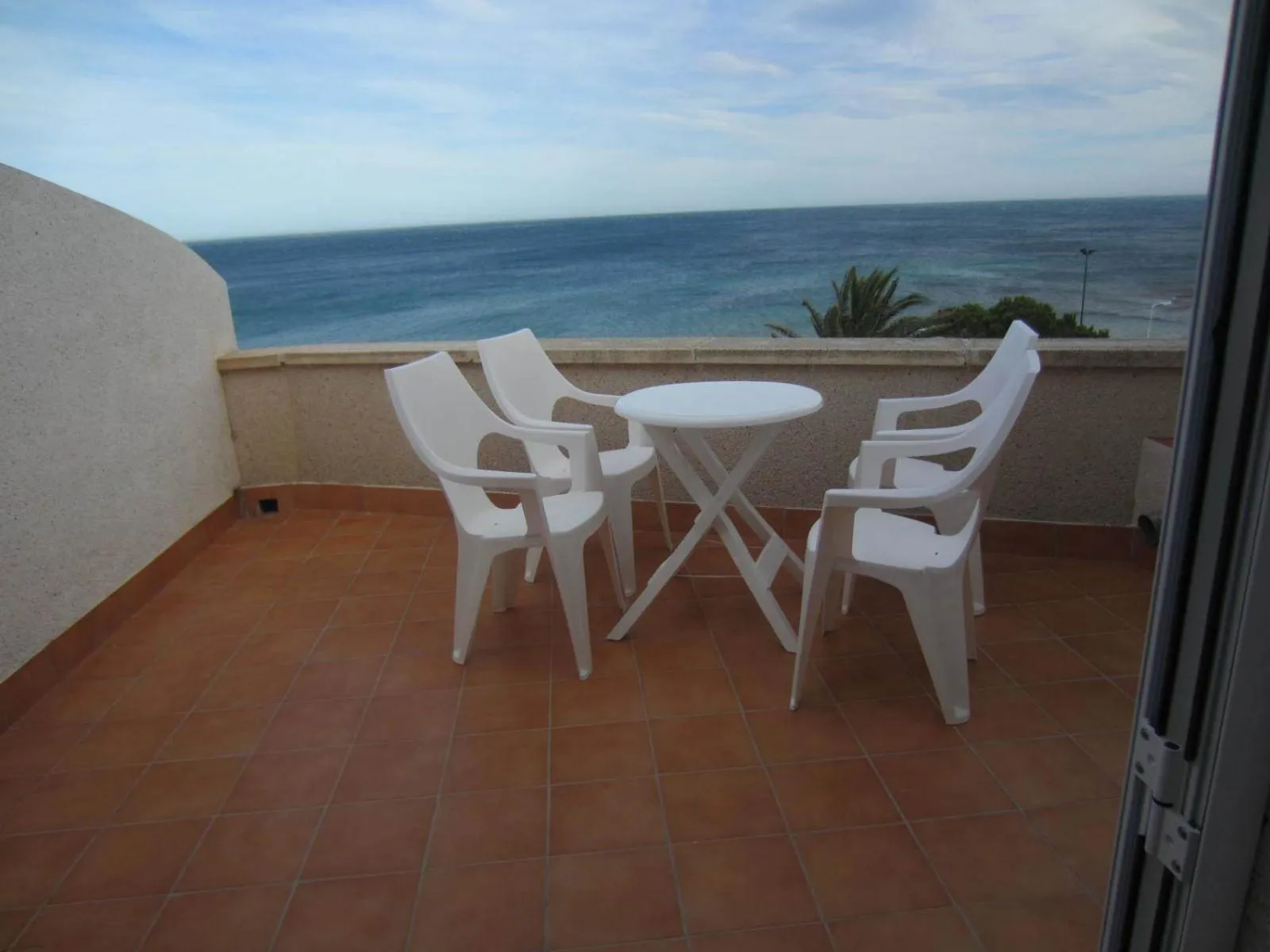 Terrasse carrelée avec mobilier en plastique blanc donnant sur la mer.