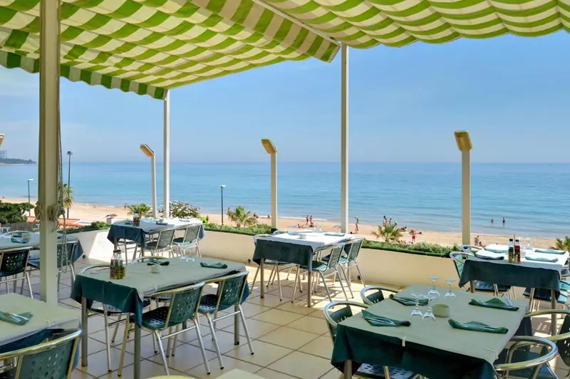 Terrasse ombragée avec tables dressées face à la mer.