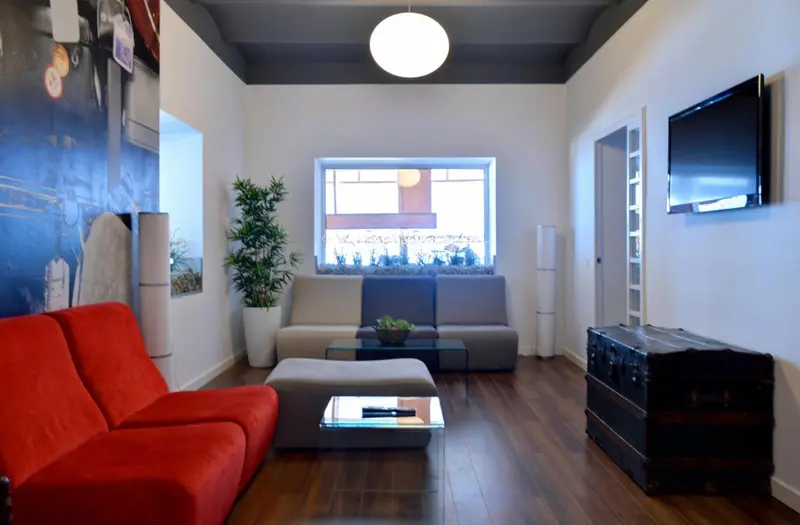 Un salon moderne avec canapés rouges et gris, une table basse en verre et une plante verte.