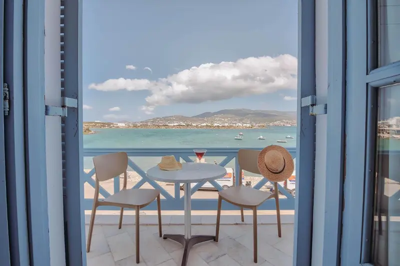Une table et deux chaises sur un balcon offrent une vue sur la mer et le ciel nuageux.