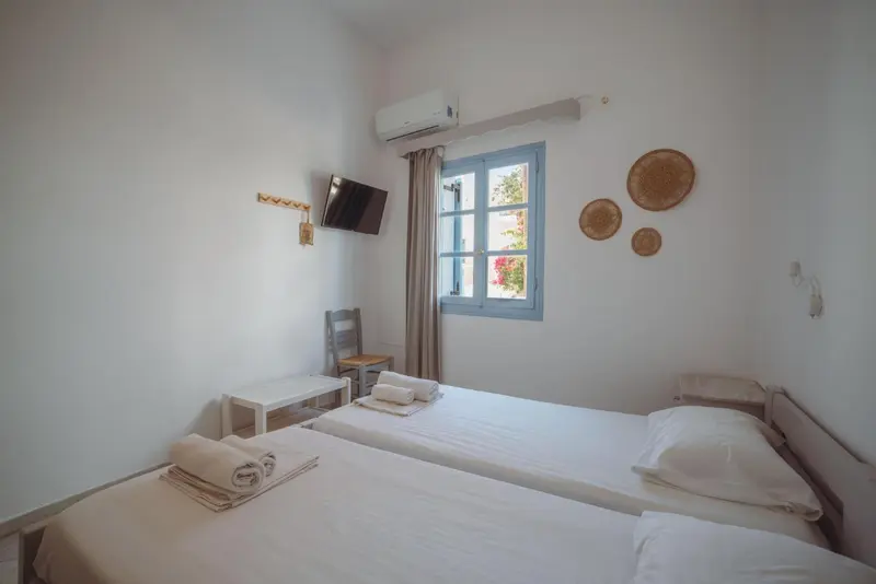 Une chambre lumineuse avec un lit simple et une télévision murale.