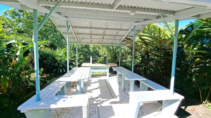Tables et bancs en bois sous une structure abritée dans un jardin tropical.