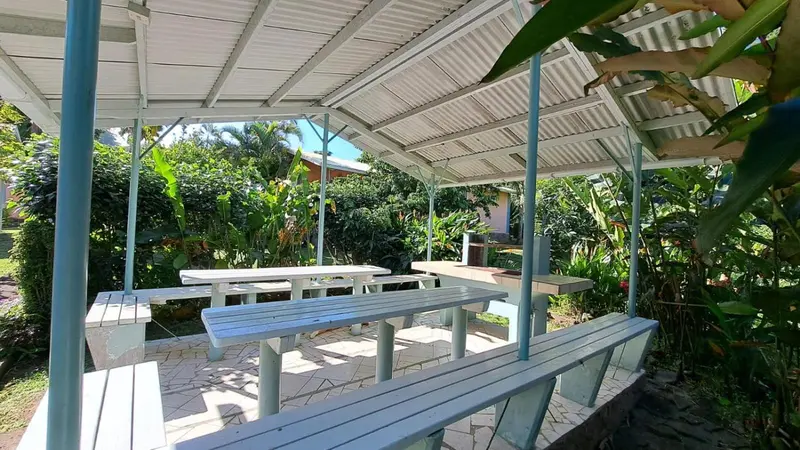 Espace repas extérieur couvert avec tables et bancs en bois.
