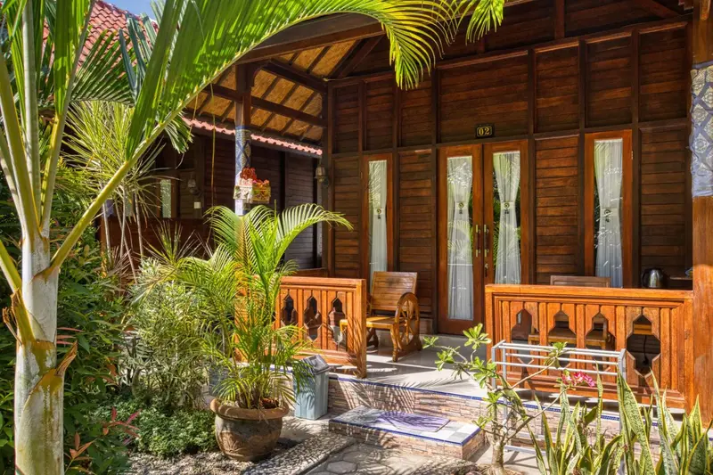Façade d'un bungalow en bois avec une terrasse et de la végétation tropicale.