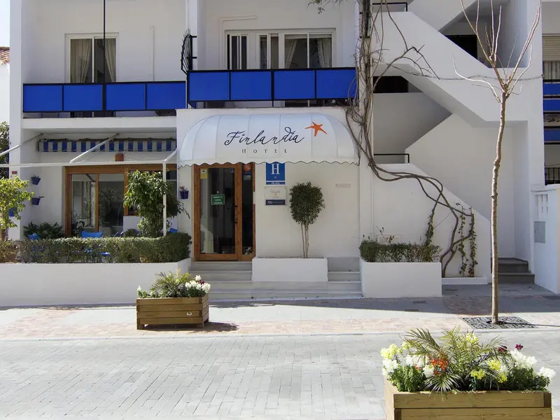 Façade blanche d'un bâtiment avec des balcons bleus et une entrée ombragée.