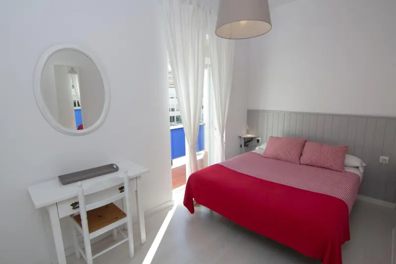 Une chambre lumineuse avec un lit rouge et un miroir rond.