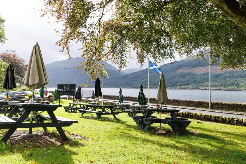 Tables en bois disposées sur une pelouse verdoyante près d'un lac de montagne.