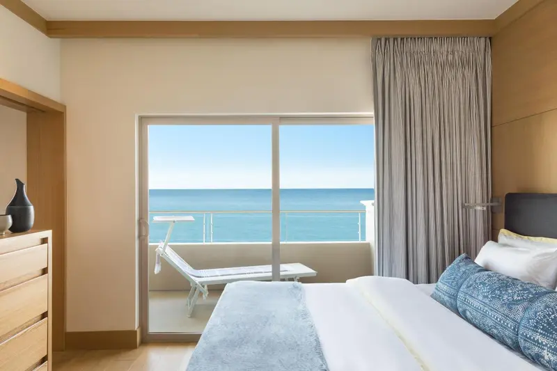 Une chambre lumineuse avec un grand lit donnant sur une vue mer depuis un balcon.