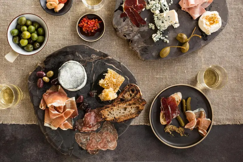 Assortiment de charcuteries, fromages et olives présentés sur des planches en ardoise et des assiettes.