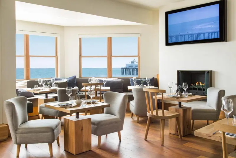 Une salle lumineuse avec des tables dressées face à une vue sur la mer.