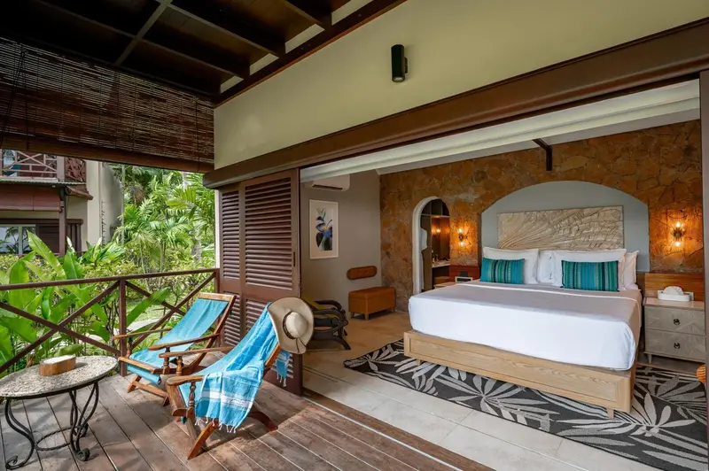 Une chambre lumineuse s'ouvre sur une terrasse avec des fauteuils.