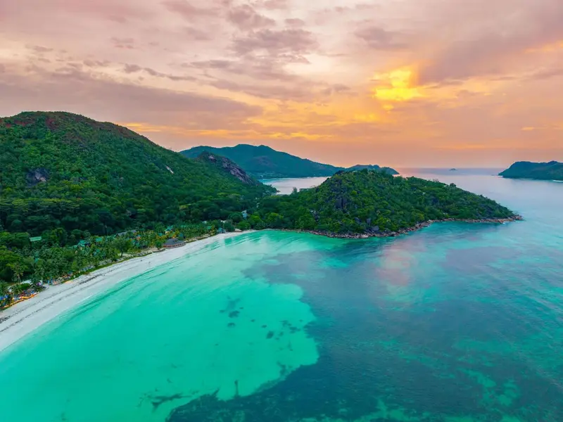 Vue aérienne d'une plage de sable blanc bordée de végétation luxuriante et d'eaux turquoise.