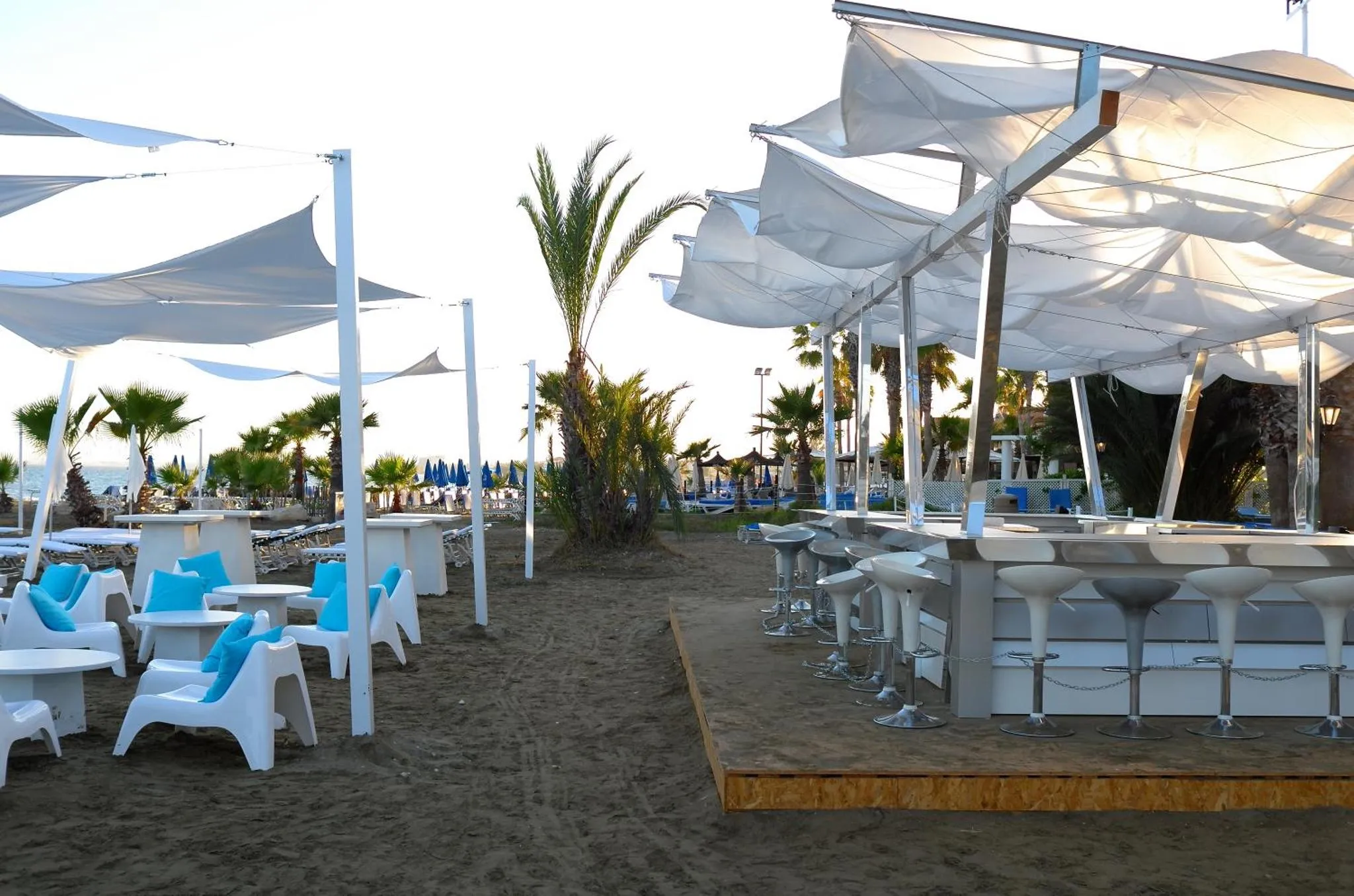 Terrasse ombragée avec mobilier de bar et transats sur une plage de sable.